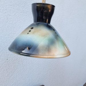 Könnte beinhalten: Eine Keramik-Pendelleuchte mit schwarzer, blauer und weißer Glasur. Die Leuchte hängt an einem Seil.
