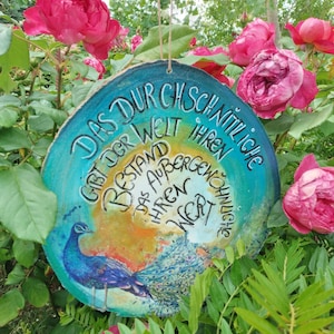 Può includere: Un cartello rotondo in legno con sfondo blu, verde e giallo. Il cartello presenta un'illustrazione di pavone e il testo "Das dur gschnitliche gibt der welt ihren bestand das aufbergen ihren wert" in scrittura corsiva nera.