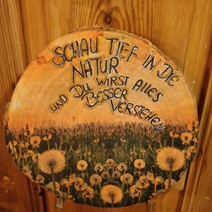 Puede incluir: Un letrero redondo de madera con el texto en alemán "SCHAU TIEF IN DIE NATUR UND DU WIRST ALLES BESSER VERSTEHEN". El letrero presenta una escena de puesta de sol con dientes de león.