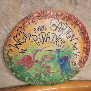 Puede incluir: Un letrero redondo de madera con una escena pintada de dos pájaros en un jardín. El letrero dice "Wer einen Garten hat lebt schon im Paradies".