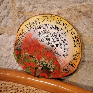 May include: A round wooden sign with a painted image of a bicycle with a basket of flowers in a field of red poppies. The sign has a handwritten message in German that reads "Zeit denn du lebst nur heute, morgen kannst du nicht nachholen und später ist trüher als du denkst".
