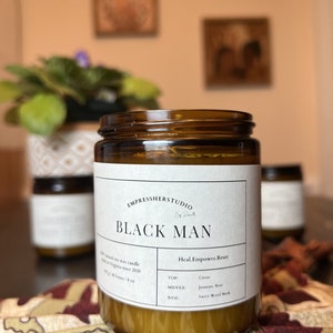 May include: A brown glass candle jar with a white label that reads "EMPRESSHERSTUDIO" and "BLACK MAN". The label also includes the text "Heal. Empower. Reset" and lists the candle's scent notes: "TOP: Citrus", "MIDDLE: Jasmine, Rose", and "BASE: Sweet Wood Musk".