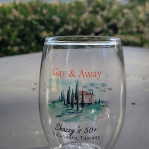 May include: A clear glass wine tumbler with a watercolour design of a Tuscan landscape and the text "Gay & Away" and "Shazzy's 50+ Villa Laura, Tuscany 2022".