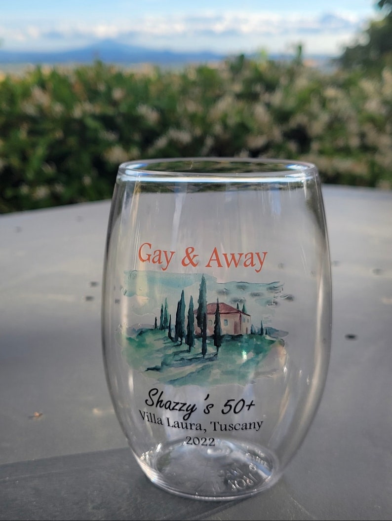May include: A clear glass wine tumbler with a watercolour design of a Tuscan landscape and the text "Gay & Away" and "Shazzy's 50+ Villa Laura, Tuscany 2022".