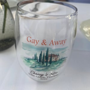 May include: A clear glass with a watercolour design of a house and trees. The text "Gay & Away" is printed on the glass. The text "Shazzy's 50+ Villa Laura, Tuscany 2022" is also printed on the glass.
