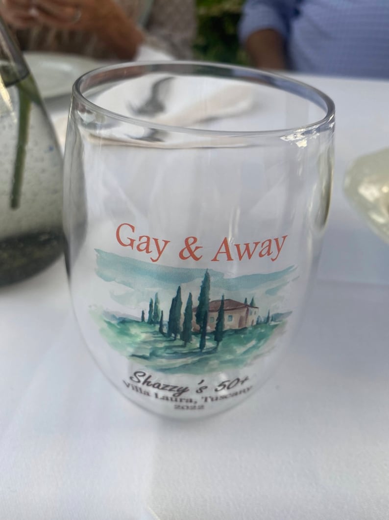 May include: A clear glass with a watercolour design of a house and trees. The text "Gay & Away" is printed on the glass. The text "Shazzy's 50+ Villa Laura, Tuscany 2022" is also printed on the glass.
