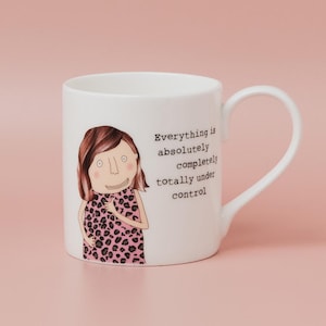 May include: White ceramic mug with a cartoon illustration of a woman in a pink leopard print dress. The mug has the text "Everything is absolutely completely totally under control". The mug has a curved handle.