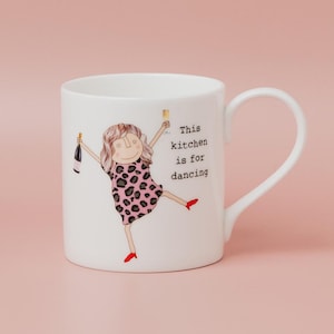 May include: White ceramic mug featuring a cartoon woman in a pink leopard print dress, holding a champagne bottle and glass. The mug has the text: "This kitchen is for dancing."