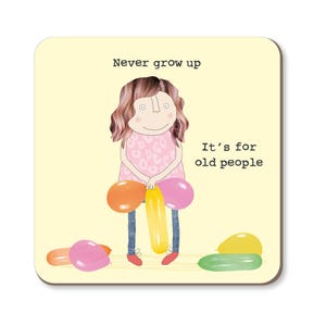May include: A square coaster featuring a cartoon illustration of a person holding balloons. The text on the coaster reads "Never grow up. It's for old people." The person is wearing a pink dress and blue jeans. Several balloons are scattered around the person.