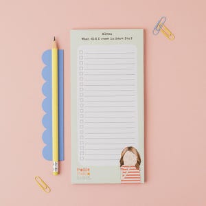 Peut inclure: Un bloc-notes vert clair avec le texte "Alexa What did I come in here for ?" et une illustration de fille. Un crayon jaune et une règle bleue sont à gauche. Deux trombones sont en haut et en bas.