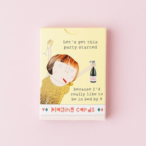 May include: A rectangular deck of playing cards in a yellow box featuring an illustration of a person with brown hair wearing a gold top, holding a champagne glass and a bottle labelled FIZZ, with the text Let's get this party started because I'd really like to be in bed by 9.