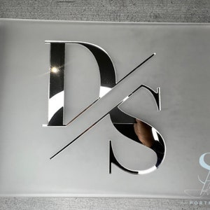May include: A frosted glass photo album with silver metal accents and a silver metallic monogram of the letters "DS" on the front. The album has a silver metal ring binding.