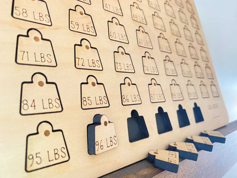 May include: A wooden board with a grid of numbered weight tags. The tags are labeled in pounds from 58 to 96. The board is made of light wood and has a black border around each tag. The tags are missing from the board and are shown below the board. The tags are black and have white text.
