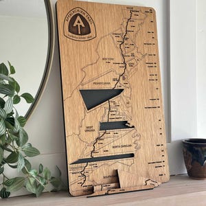 May include: Wooden Appalachian Trail map with engraved states and trail route. Features the Appalachian Trail logo and state names. Includes a stand for display. A decorative piece for hikers.