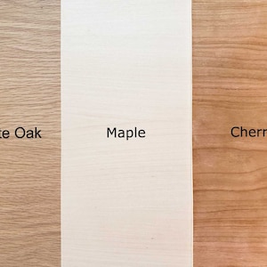 May include: Close-up of three wood samples: white oak, maple, and cherry. The wood grain is visible in each sample.