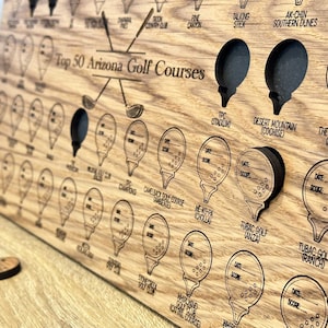 May include: A wooden board with a list of the top 50 Arizona golf courses. Each course is represented by a golf ball icon with a space to record the date and score. The board is made of a light brown wood with a dark brown stain.