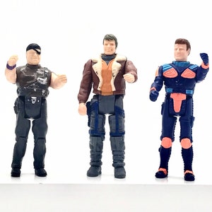 May include: Three action figures, one wearing a brown leather jacket, one wearing a black and blue suit, and one wearing a black shirt and pants.