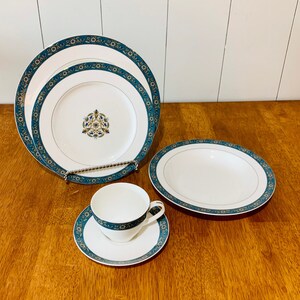 May include: A set of white porcelain dinnerware with a blue and gold floral pattern. The set includes a dinner plate, a salad plate, a soup bowl, a teacup, and a saucer.