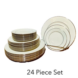 May include: A 24-piece white dinnerware set with gold trim. The set includes multiple plates of varying sizes, stacked in two separate groups. The plates are displayed on a white background.