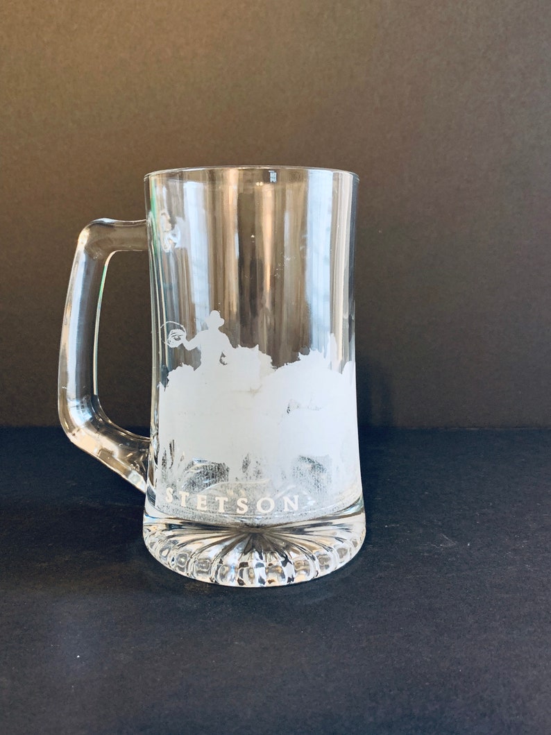 Peut inclure: Mug &agrave; bi&egrave;re en verre transparent avec une anse. Le mug pr&eacute;sente un motif givr&eacute; d'un cow-boy attrapant un taureau, avec le mot "STETSON" en dessous. La base du mug a un motif d&eacute;coratif &agrave; nervures.