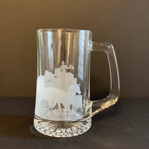 Peut inclure: Mug &agrave; bi&egrave;re en verre transparent avec une anse et un motif grav&eacute;. Le motif repr&eacute;sente un cow-boy attrapant un taureau avec un lasso, avec des chevaux en arri&egrave;re-plan. Le mug a une base textur&eacute;e.
