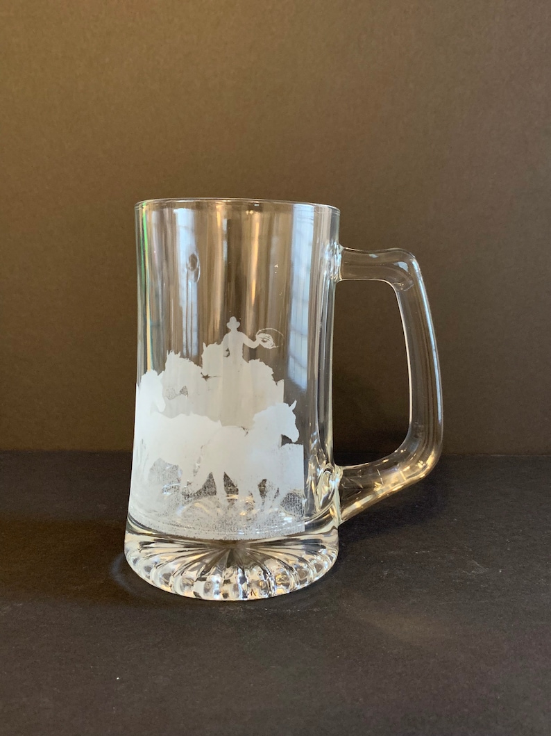 Peut inclure: Mug &agrave; bi&egrave;re en verre transparent avec une anse et un motif grav&eacute;. Le motif repr&eacute;sente un cow-boy attrapant un taureau avec un lasso, avec des chevaux en arri&egrave;re-plan. Le mug a une base textur&eacute;e.
