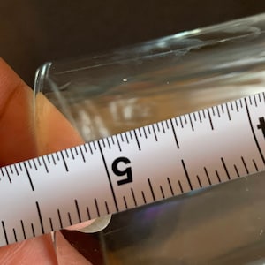 Peut inclure: Un objet clair et rectangulaire est mesur&eacute; avec une r&egrave;gle blanche. La r&egrave;gle indique une mesure d'environ 12,7 cm. L'objet est transparent et semble &ecirc;tre en verre ou dans un mat&eacute;riau similaire.