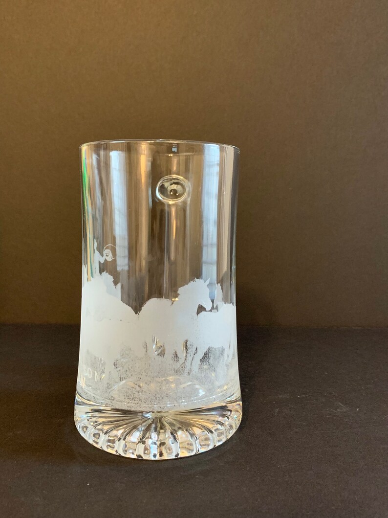 Peut inclure: Verre &agrave; boire transparent avec un motif givr&eacute; de chevaux au galop. Le verre a une base arrondie avec des rainures verticales et une petite bulle sur le c&ocirc;t&eacute;. Le motif est grav&eacute; dans le verre, cr&eacute;ant un aspect blanc textur&eacute;.
