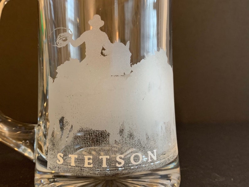 Peut inclure: Mug &agrave; bi&egrave;re en verre transparent avec une anse, orn&eacute; d'un motif givr&eacute; d'un cow-boy &agrave; cheval. Le mot "STETSON" est imprim&eacute; en blanc au bas du mug.