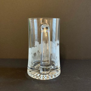 Peut inclure: Chope &agrave; bi&egrave;re en verre transparent avec une anse et un motif grav&eacute; de chevaux au galop. La chope a une base &eacute;paisse et textur&eacute;e et une anse transparente. Le motif grav&eacute; est visible sur le devant.