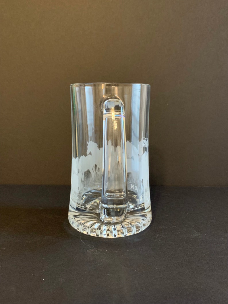 Peut inclure: Chope &agrave; bi&egrave;re en verre transparent avec une anse et un motif grav&eacute; de chevaux au galop. La chope a une base &eacute;paisse et textur&eacute;e et une anse transparente. Le motif grav&eacute; est visible sur le devant.