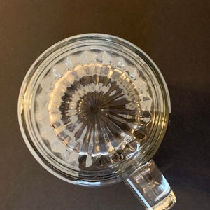 Peut inclure: Mug &agrave; boire en verre transparent avec une poign&eacute;e, vue de dessus. Le fond du mug pr&eacute;sente un motif textur&eacute; et nervur&eacute;. Le mug est pos&eacute; sur une surface sombre.