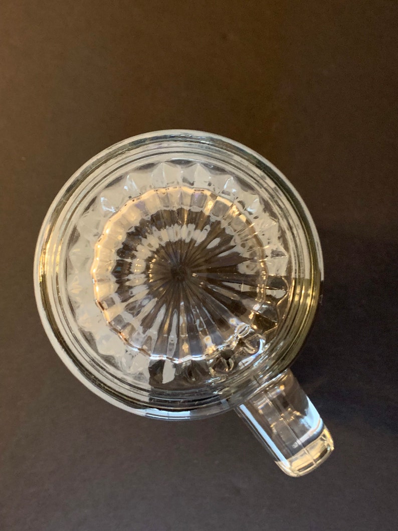Peut inclure: Mug &agrave; boire en verre transparent avec une poign&eacute;e, vue de dessus. Le fond du mug pr&eacute;sente un motif textur&eacute; et nervur&eacute;. Le mug est pos&eacute; sur une surface sombre.