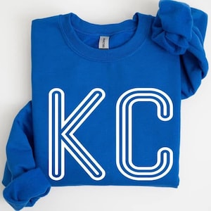 May include: A royal blue sweatshirt with a white outline of the letters "KC" on the front.
