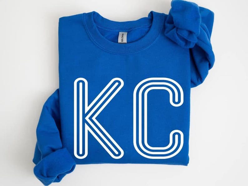 May include: A royal blue sweatshirt with a white outline of the letters "KC" on the front.
