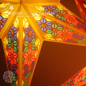 K&ouml;nnte beinhalten: Eine gro&szlig;e, mehrfarbige Papierlaterne in Form eines Sterns mit einem geometrischen Muster. Der Stern ist von innen beleuchtet und strahlt ein warmes Licht aus. Der Text "paperstarlights Handmade Natural & Ethical" ist auf dem Stern sichtbar.