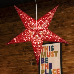 May include: A red paper star lantern with a white and gold patterned design. The star is hanging from the ceiling and is illuminated from within.