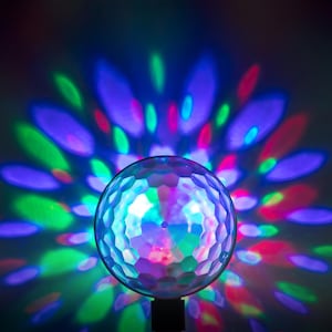 Op de afbeelding: Een facet disco-bal met een zwarte basis, die kleurrijke lichtpatronen in blauw, groen, paars en rood projecteert. De bal is verlicht, waardoor een levendige en dynamische weergave ontstaat. Perfect voor feesten en evenementen.
