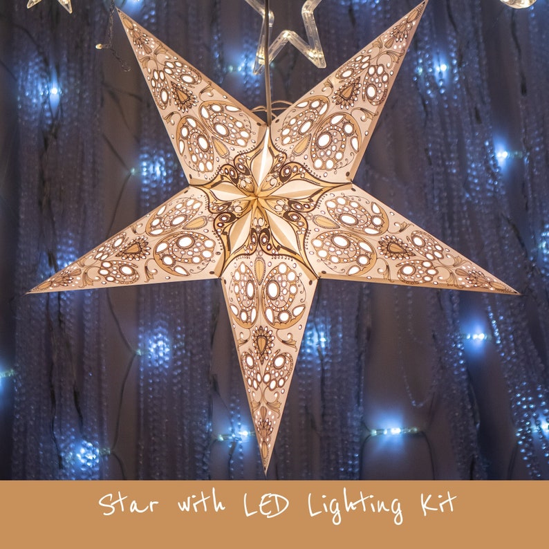 May include: A white paper star with a gold and white patterned design. The star is illuminated with LED lights and hangs from a string. The background is a dark blue with white lights.