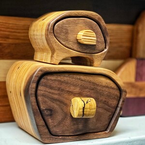 May include: Two wooden boxes with intricate designs and unique drawer pulls. The top box is made of light wood with a dark wood drawer, while the bottom box is made of dark wood with a light wood drawer.