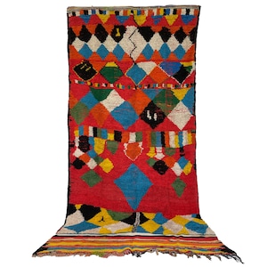May include: A colorful Moroccan rug with a geometric diamond pattern in shades of red, blue, green, yellow, black, and white. The rug has a fringe border.