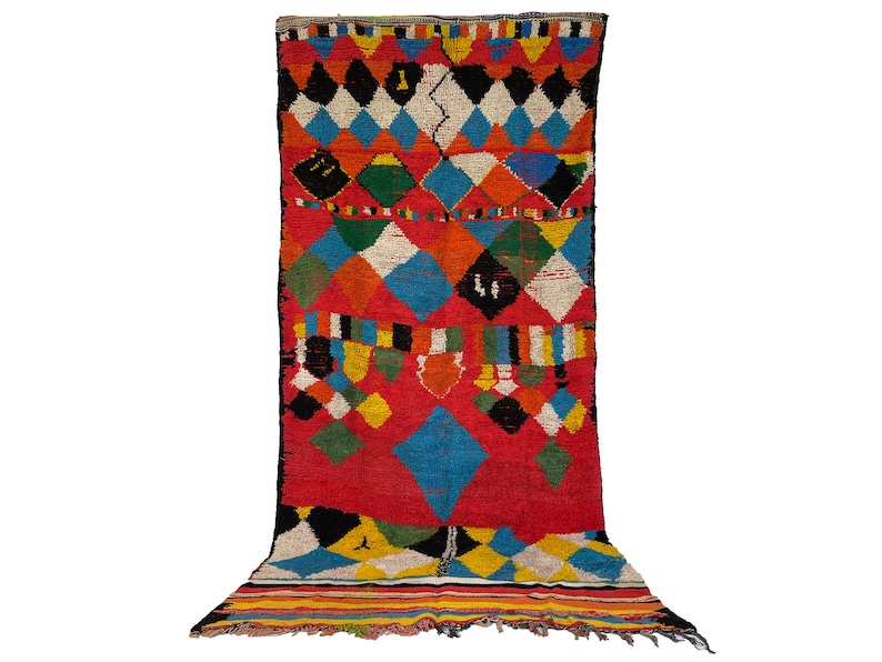 May include: A colorful Moroccan rug with a geometric diamond pattern in shades of red, blue, green, yellow, black, and white. The rug has a fringe border.