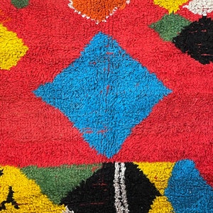 May include: A colorful rug with geometric shapes in shades of red, blue, yellow, green, black, and white. The rug has a fuzzy texture.