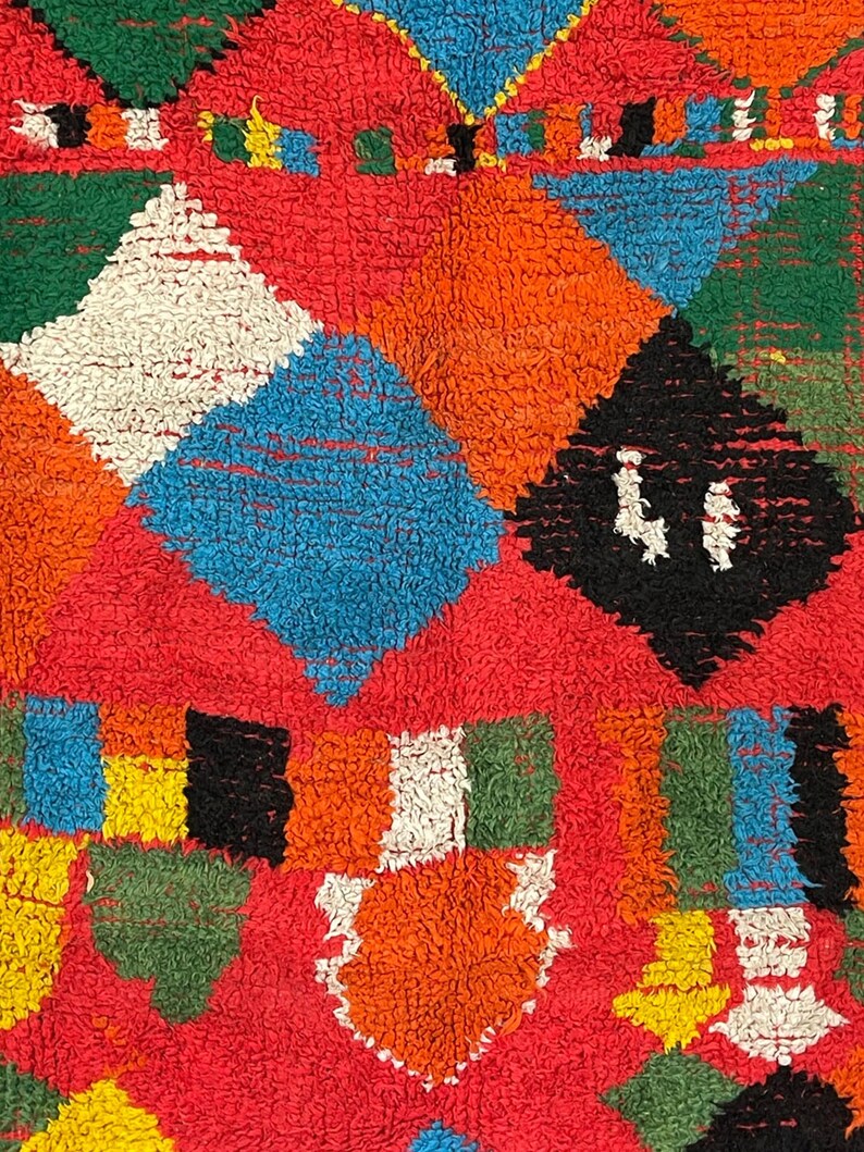 May include: A colorful rug with a geometric pattern in shades of red, orange, blue, green, white, and black. The rug is made of a soft, fluffy material.