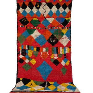 May include: A colorful Moroccan rug with a diamond pattern in shades of red, blue, green, yellow, black, and white. The rug has a fringe border.