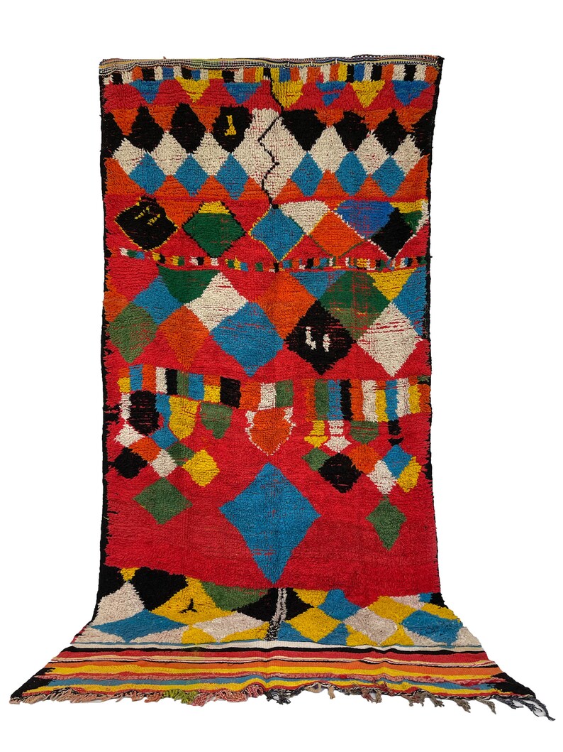 May include: A colorful Moroccan rug with a diamond pattern in shades of red, blue, green, yellow, black, and white. The rug has a fringe border.