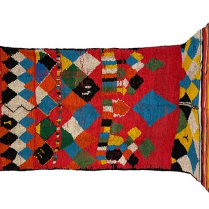 May include: A colorful Moroccan rug with a geometric pattern of diamonds and squares in shades of red, blue, yellow, green, and black. The rug has a fringe border.