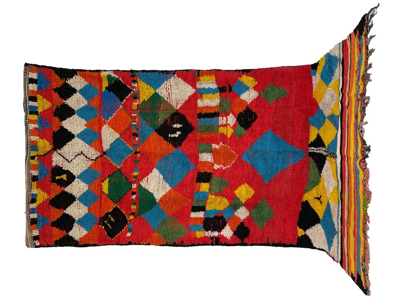 May include: A colorful Moroccan rug with a geometric pattern of diamonds and squares in shades of red, blue, yellow, green, and black. The rug has a fringe border.