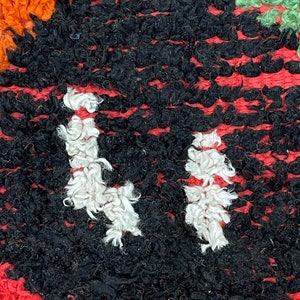May include: Close-up of a black and white rug with a red border. The rug is made of thick, fuzzy yarn and has a unique pattern.