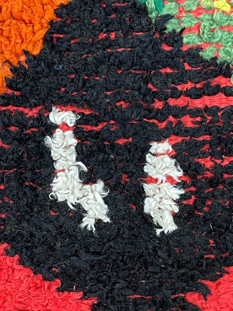 May include: Close-up of a black and white rug with a red border. The rug is made of thick, fuzzy yarn and has a unique pattern.
